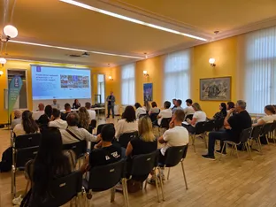 Raznolikost vodenih programov v 12 slovenskih regijah je predstavljena na projekciji, medtem ko poslušalci sedijo v stolih.
