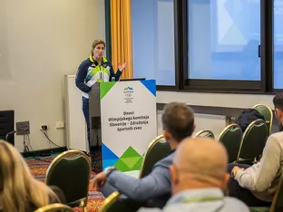 Ženska v športni obleki govori za mizo z napisom "Dnevi Olimpijskega komiteja Slovenije - Združenja športnih zvez".