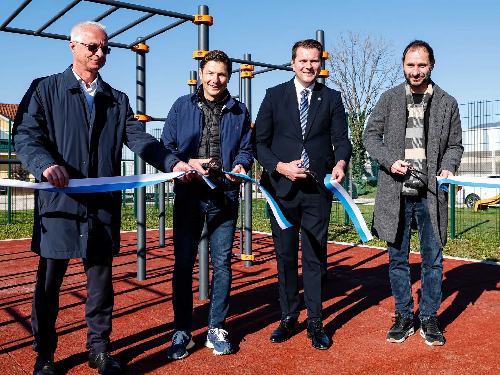 Četverica moških drži trakove, pripravljeni na rezanje ob novem športnem poligonu.