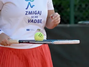 Ženska v beli majici z napisom "ZMIGAJ SE DO VADBE" drži teniško lopar in se pripravlja na udarec žoge.