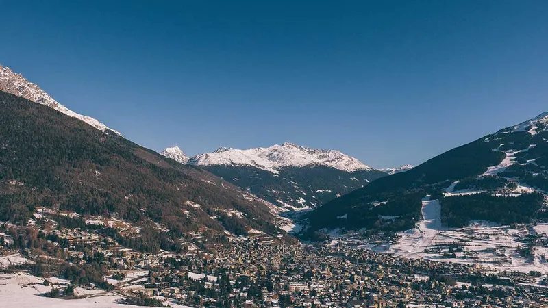 Zasnežena pokrajina z gorami v ozadju in naseljem v dolini.