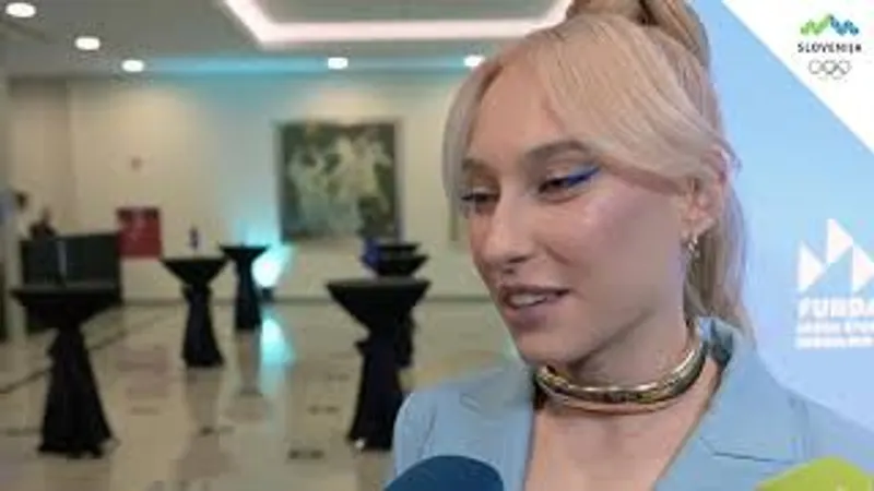 Ženska z dolgimi svetlimi lasmi in modrim ličilom na očeh govori v mikrofon.