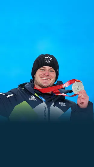 Tim Mastnak z nasmehom pozira s srebrno medaljo in šopkom ob ozadju z napisom Beijing 2022, kot simbol uspeha v deskanju na snegu v disciplini paralelni veleslalom